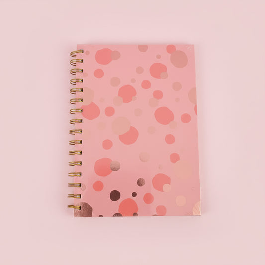 Pink spiral-bound notebook with a polka dot pattern on a black surface.