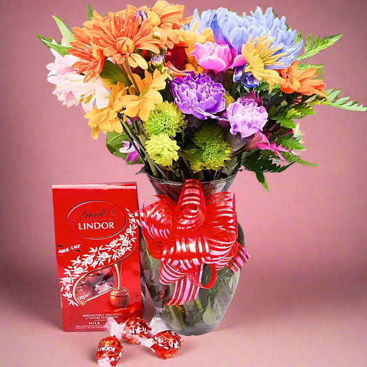 Bouquet of colorful flowers with a red Lindor chocolate box on a wooden surface.