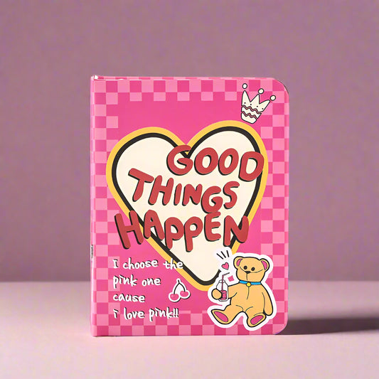 Pink checkered notebook with 'Good Things Happen' text and cartoon bear on a white background