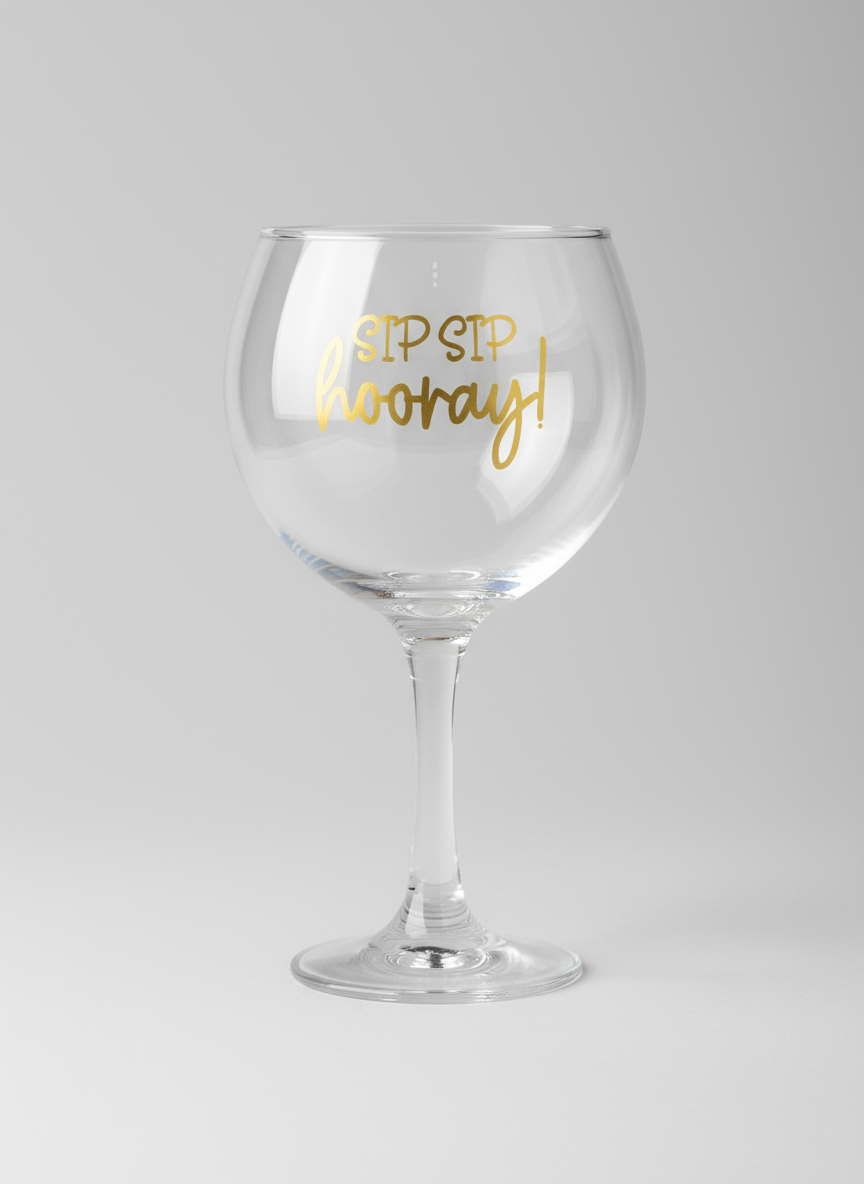 Clear wine glass with 'Sip Sip Hooray!' text in gold on a white background