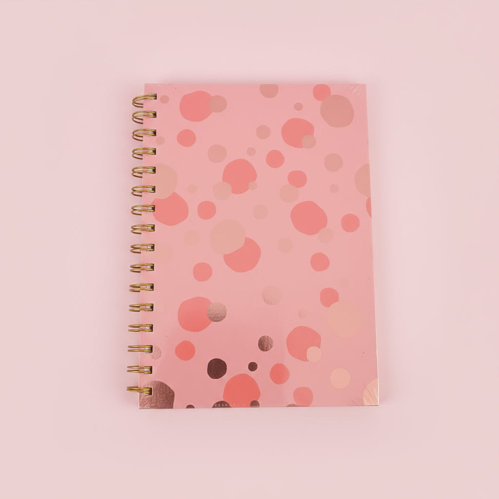 Pink spiral-bound notebook with a polka dot pattern on a black surface.