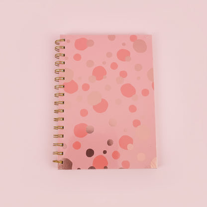 Pink spiral-bound notebook with a polka dot pattern on a black surface.